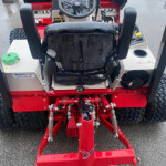 Front view of a red industrial tractor-like machine with a black seat and steering wheel, wet from rain and ready for operation at a hitch-equipped front frame.