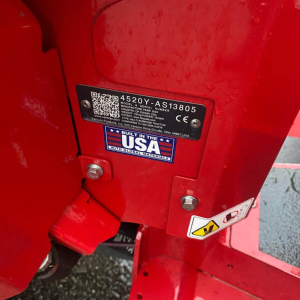Close-up of a red farming implement with a metal data plate listing model/serial number and a 'Built in the USA' sticker, bolts visible nearby.