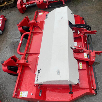Red agricultural implement with a silver protective cover lying on wet pavement, showing warning labels and hydraulic hoses.
