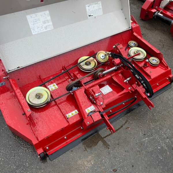 Red farming implement with belt-driven pulleys and a large grey guard, mounted on a red chassis, sitting on a wet asphalt surface.