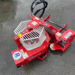 Red industrial machine with metal basket and black wrapped hoses on wet asphalt surface.