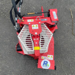 Top view of a red stump grinder attachment with safety guards, hoses, and a Russell's logo on a wet asphalt surface.