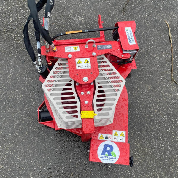 Top view of a red stump grinder attachment with safety guards, hoses, and a Russell's logo on a wet asphalt surface.