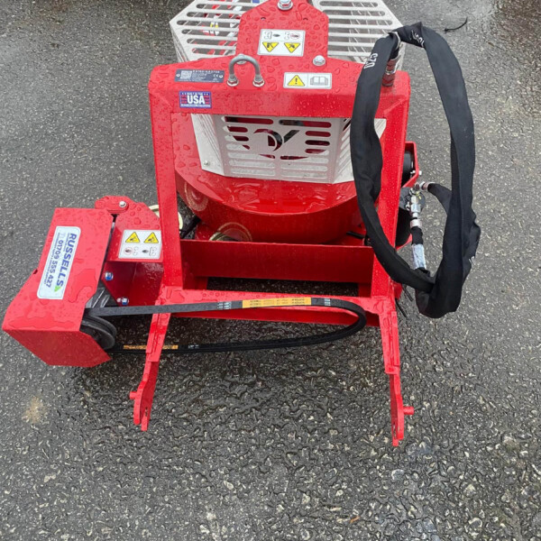 Red portable hydraulic power unit with hoses and metal grate frame, sitting on wet asphalt; safety labels and a U.S. flag sticker visible.
