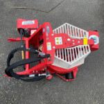 Red industrial cart with a white grated basket on wet asphalt; a long brown stick lies above it.