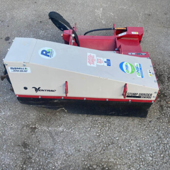 Red stump grinder attachment on a trailer resting on rough pavement; branding includes DENTRAC and KC220 model label on the side.