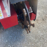 Close-up of a red farming machine's rusted track and linkage, showing worn metal rollers and bolts.