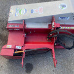 Red agricultural implement with hoses, stickers and warning labels on a gravel surface.