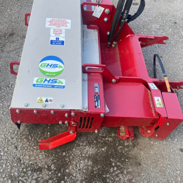 Top-down view of a red and gray industrial machine on a gravel surface, showing hydraulic hoses and warning stickers on the unit.