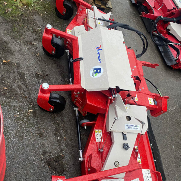 Red industrial log-splitting or wood-processing attachment on wheels, with hydraulic arms and control levers visible. Brand stickers and warning labels on the silver panels.