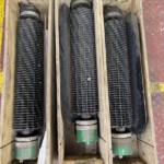 Three long black corrugated rollers mounted in wooden crates on a diamond-plate floor, likely part of a conveyor system.