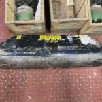 Two wooden crates containing green cylindrical components sit on a dirty red diamond-plate workshop floor outside a machine area.