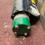 Close-up of a green hydraulic coupling attached to a cylindrical metal tool on a red diamond-plate floor.