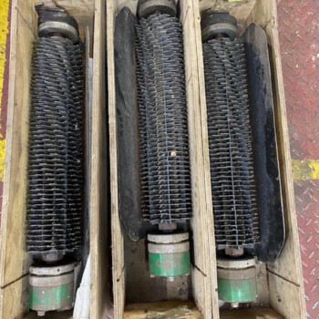 Three long black corrugated rollers mounted in wooden crates on a diamond-plate floor, likely part of a conveyor system.