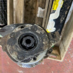 Close-up of a dusty black circular mechanical hub with a central hollow bore, mounted to a metal bracket in a workshop.