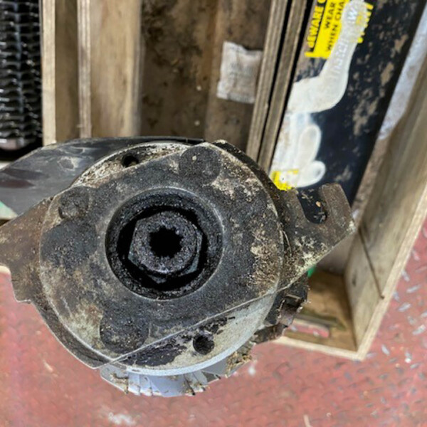 Close-up of a dusty black circular mechanical hub with a central hollow bore, mounted to a metal bracket in a workshop.
