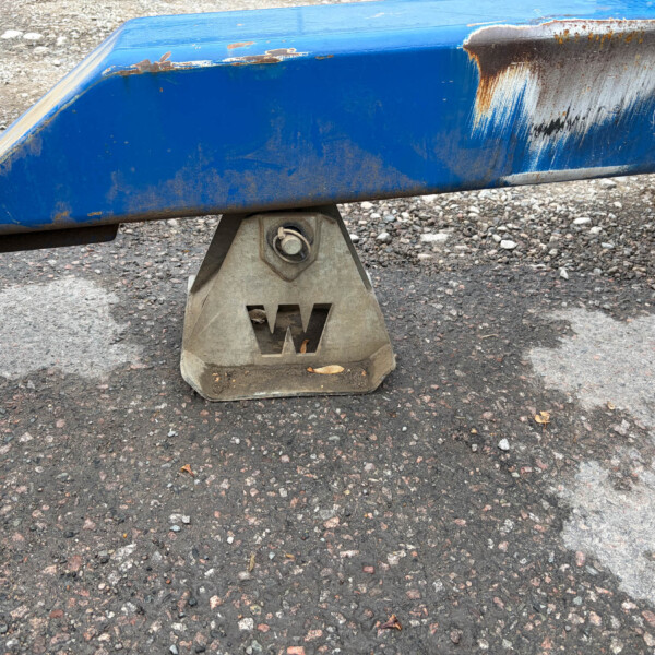 Blue boat hull resting on a concrete stand, with rust and chipped paint on a gravel surface