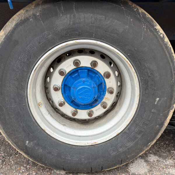 Close-up of a large truck tire with a blue hub and white rim, dirt on the tire surface and ground nearby.