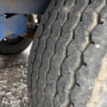 Close-up of a large tire tread with dirt, beside a blue metal frame.