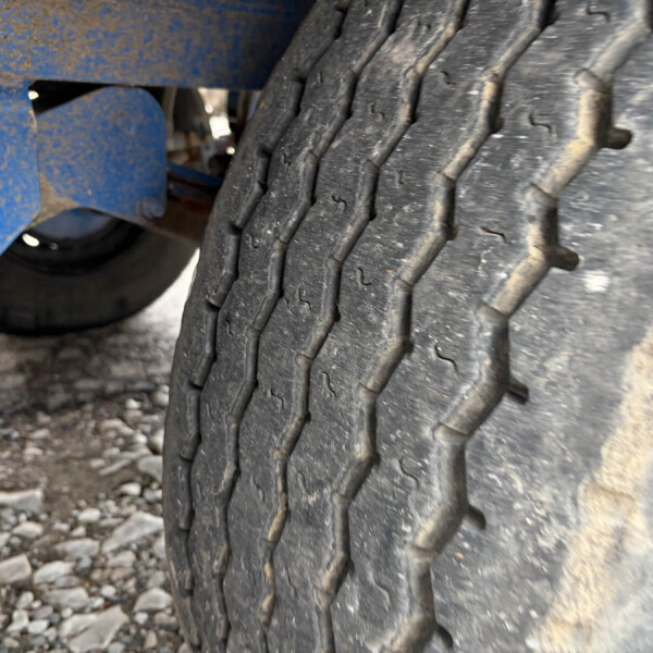 Close-up of a large tire tread with dirt, beside a blue metal frame.