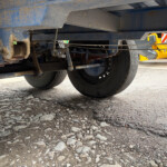 Underside of a blue trailer showing axles, suspension and wheels on a rocky surface.
