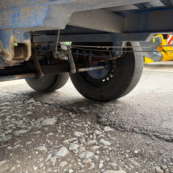 Underside of a blue trailer showing axles, suspension and wheels on a rocky surface.