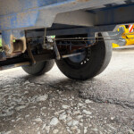 Underside of a heavy dump truck showing suspension and wheels on a gravel surface.