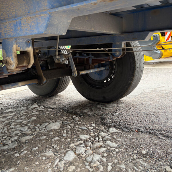 Underside of a heavy dump truck showing suspension and wheels on a gravel surface.