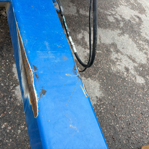 Close-up of a weathered blue metal beam with rust spots, resting on a gravel surface with a black hydraulic hose nearby.